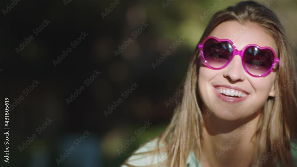 Young adult girl looking into camera and putting on heart shaped sunglasses