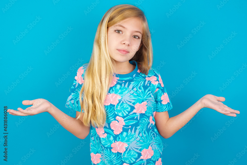 Careless attractive Caucasian kid girl wearing hawaiian T-shirt against blue wall shrugging shoulders, oops. Careless attractive Caucasian kid girl wearing hawaiian T-shirt against blue wall shrugging shoulders, oops.