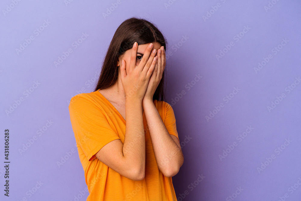 Young caucasian woman isolated on purple background blink at the camera through fingers, embarrassed covering face. Young caucasian woman isolated on purple background blink at the camera through fingers, embarrassed covering face.