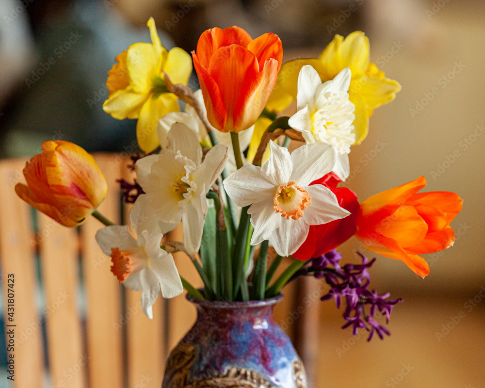 A bright spring bouquet of daffodils and tulips in a purple vase on a table. A bright spring bouquet of daffodils and tulips in a purple vase on a table.