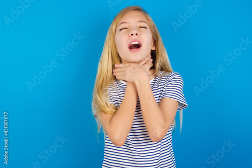 Fotografie Caucasian kid girl wearing striped shirt ​against blue wall  shouting suffocate because painful strangle