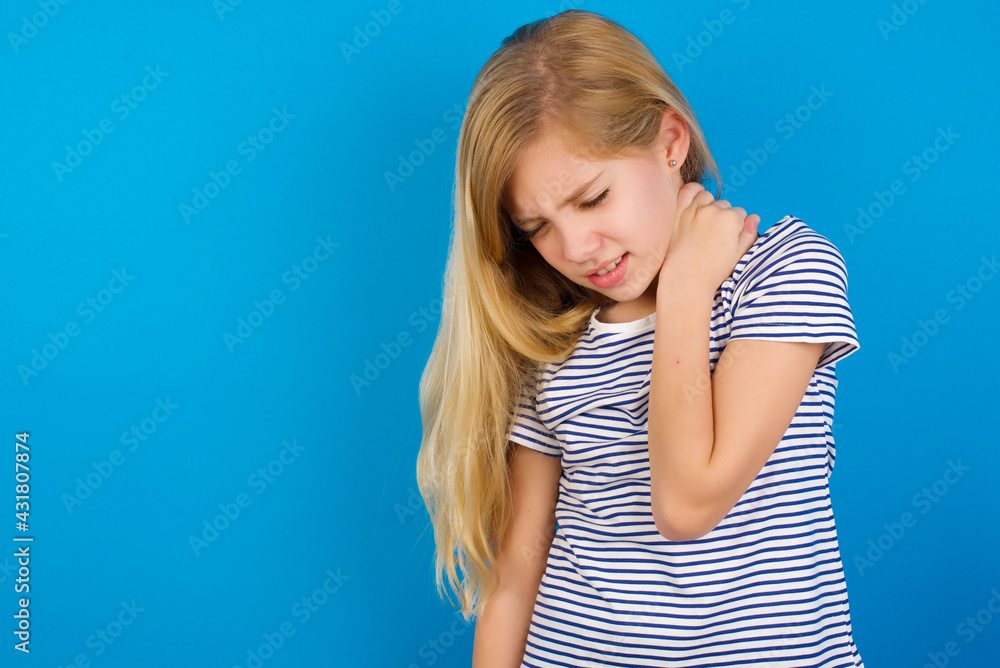 Caucasian kid girl wearing striped shirt against blue wall Suffering of neck ache injury, touching neck with hand, muscular pain Caucasian kid girl wearing striped shirt against blue wall Suffering of neck ache injury, touching neck with hand, muscular pain