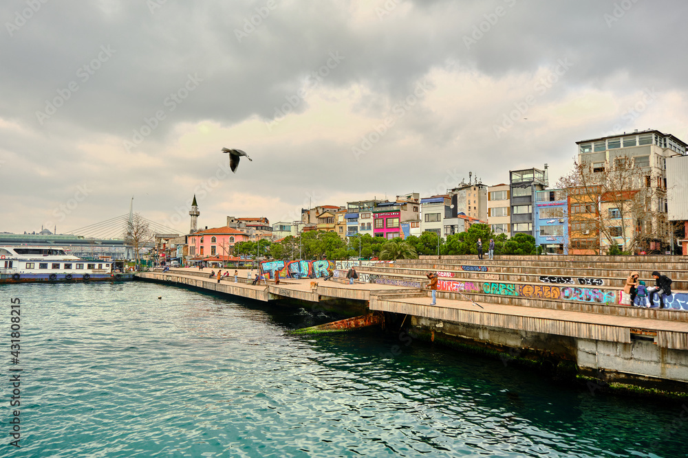 Turkey istanbul 03.03.2021. Karakoy shore and colorful painting on seating area and a man waiting for fishing with fishing rod in istanbul golden horn and bosporus and young couples talking Turkey istanbul 03.03.2021. Karakoy shore and colorful painting on seating area and a man waiting for fishing with fishing rod in istanbul golden horn and bosporus and young couples talking