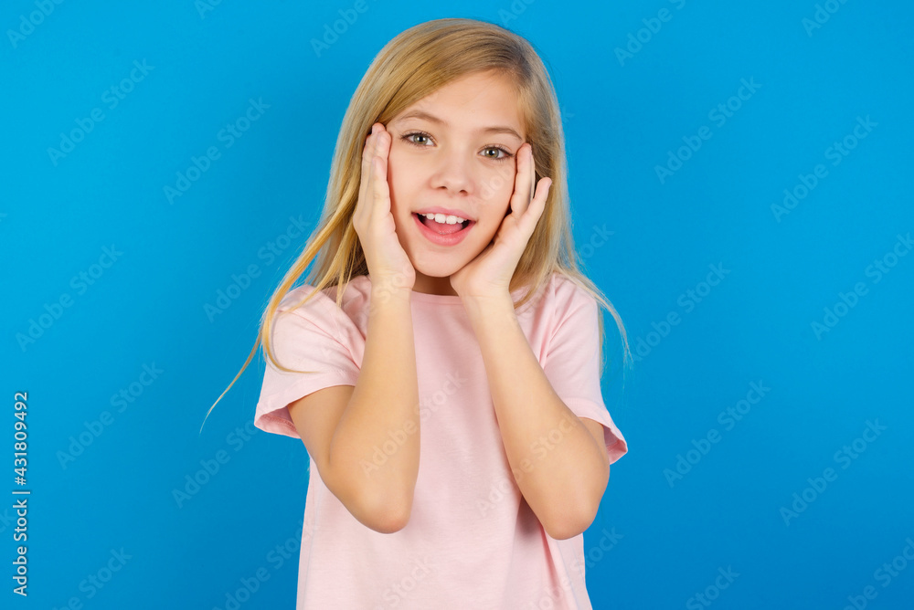 Caucasian kid girl wearing pink shirt against blue wall Pleasant looking cheerful, Happy reaction Caucasian kid girl wearing pink shirt against blue wall Pleasant looking cheerful, Happy reaction