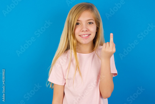 Foto Caucasian kid girl wearing pink shirt against blue wall shows middle finger bad sign asks not to bother