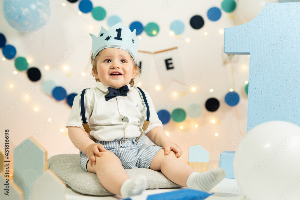 Caucasian small infant baby boy celebrating his first birthday blonde child with blue crown and number one on it one year old happy kid Caucasian small infant baby boy celebrating his first birthday blonde child with blue crown and number one on it one year old happy kid