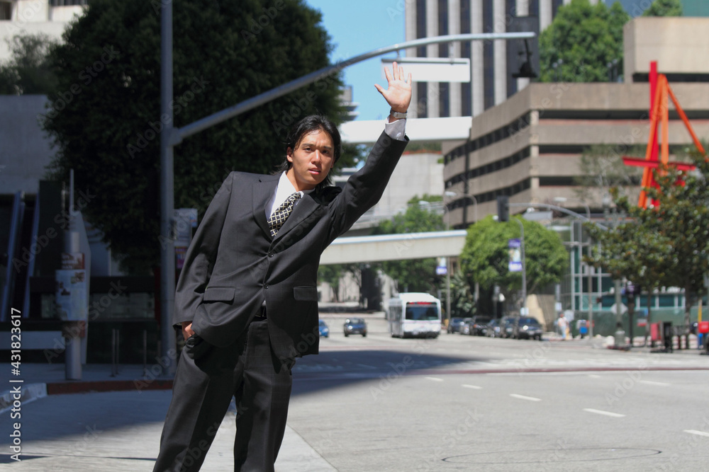 A young Japanese businessman raising his hand to stop a taxi in a business district in Los Angeles, USA A young Japanese businessman raising his hand to stop a taxi in a business district in Los Angeles, USA