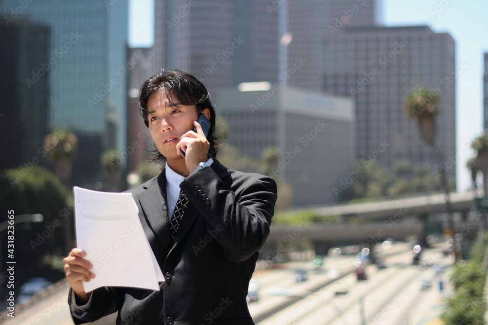 A young Japanese businessman using a mobile phone in a business district in Los Angeles, USA
