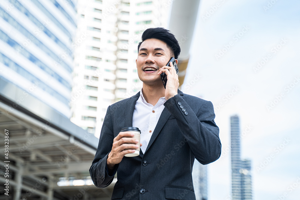 Asian young businessman talking on mobile phone, walking to the office Asian young businessman talking on mobile phone, walking to the office