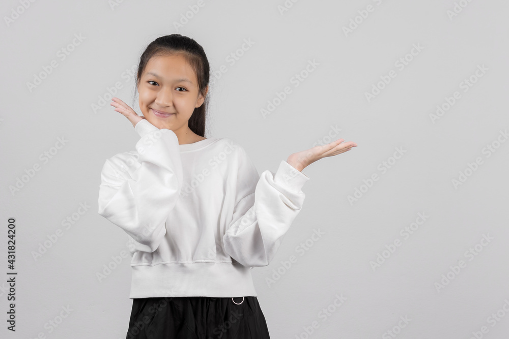 Cute little girl smiling to the camera while presenting with hand and pointing with finger on gray background