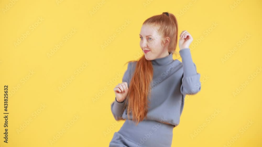 Beautiful woman with freckles and long ginger ponytail is looking into the camera, smiling and dancing in a funny way. Yellow background Beautiful woman with freckles and long ginger ponytail is looking into the camera, smiling and dancing in a funny way. Yellow background