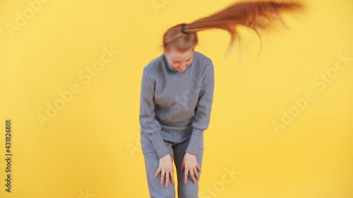 Woman with long ginger hair is twirling her ponytail in a funny way. Yellow background in studio