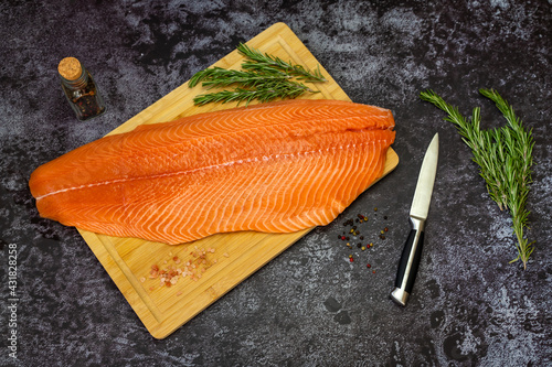 Fresh raw salmon fish fillet on a cutting board, also next to sea salt, thyme, rosemary.