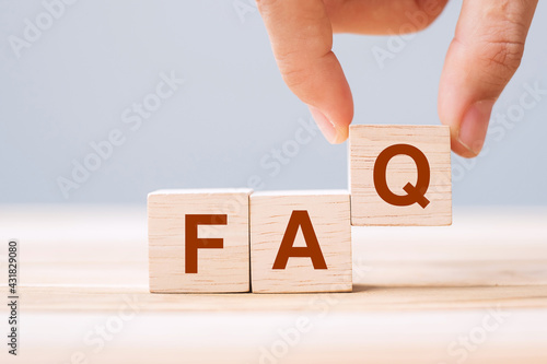 Tableau sur toile Hand holding wooden cube blocks with FAQ text (frequently asked questions) on table background