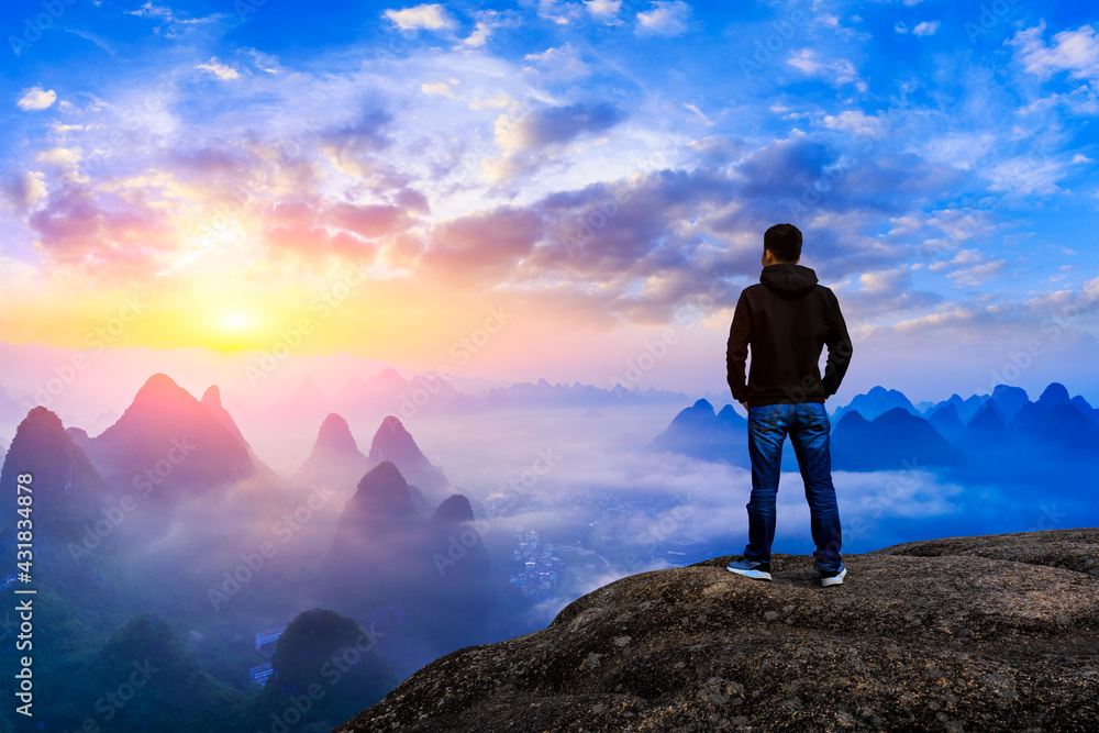 Young man standing in the summer mountains at sunrise and enjoying view of nature.