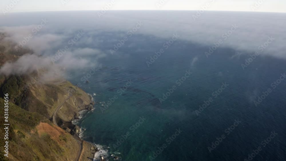 Aerial Panning High Above The Clouds And Over The Steep Mountain Shoreline Along The Pacific Ocean Coast, With Sunlight, Deep Blue Ocean Waters, And The Green Brush - Big Sur, California Aerial Panning High Above The Clouds And Over The Steep Mountain Shoreline Along The Pacific Ocean Coast, With Sunlight, Deep Blue Ocean Waters, And The Green Brush - Big Sur, California