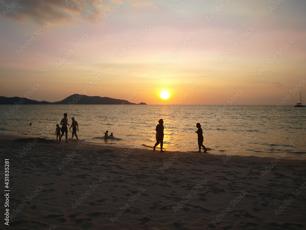 Beautiful sunset over the sea. People on the beach. Tropical resort at the evening. Patong beach, Phuket, Thailand. Silhouettes of tourists in the water. Colorful sundown, pink, yellow, orange colors 