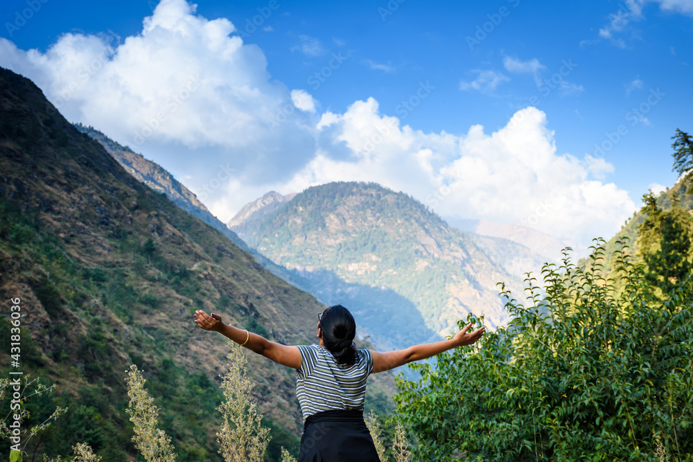 Happy woman stands with raised hands on background of sunset in mountain's range
