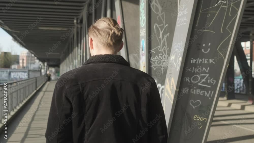 Young European Man with Man Bun, Glasses and a Black Jacket Walking on Sidewalk during Daytime in Hamburg, Germany