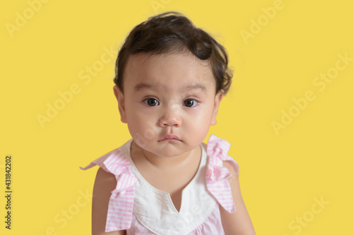 Portrait of a cute little Asian baby girl, look at camera isolated on yellow background, baby expression concept