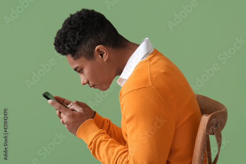 Teenage boy with bad posture using mobile phone on color background
