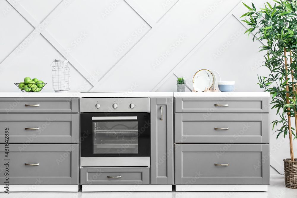 Fototapeta premium Modern furniture with oven near light wall in kitchen