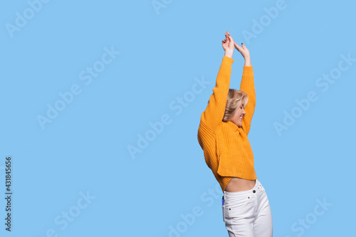 Cheering woman with blonde hair is posing on a blue wall with free space