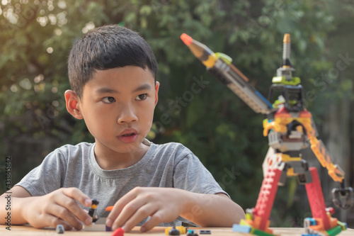 Short hair Asian boy age 7 year old play plastic toy blocks in his outdoor home garden on blurred green tree background. Image for leisure activity and recreation or stay home from COVID-19 concept.