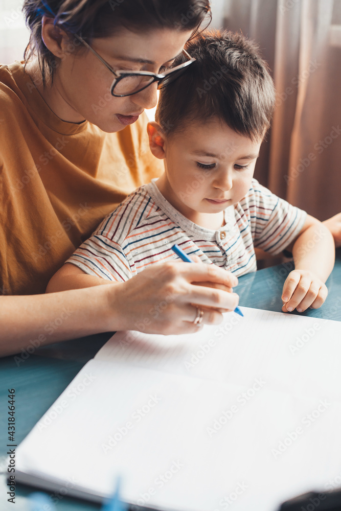 Close up photo of a caucasian mother helping her son to write at home Close up photo of a caucasian mother helping her son to write at home