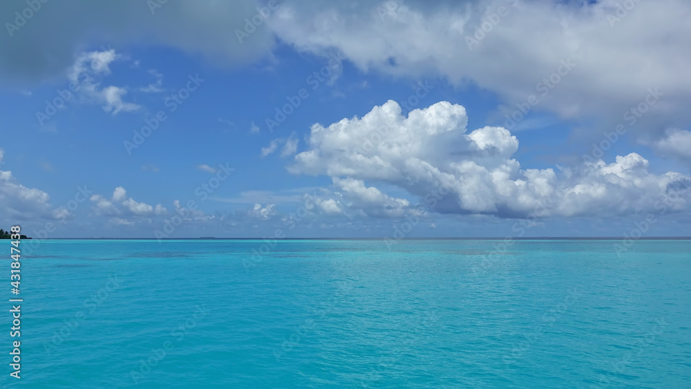 The aquamarine ocean is calm. There are picturesque cumulus clouds in the azure sky. Summer sunny day. Maldives idyll