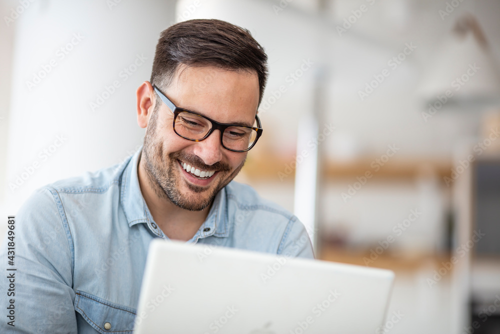 Young man working at home in the evening. Young businessman working at home using lap top. Young attractive smiling guy is browsing at his laptop, sitting at home Young man working at home in the evening. Young businessman working at home using lap top. Young attractive smiling guy is browsing at his laptop, sitting at home