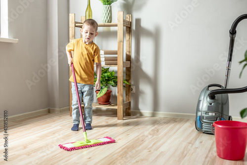 Little boy is cleaning the floor of a room using a mop. Concept of independence, help to parents, housework of the child