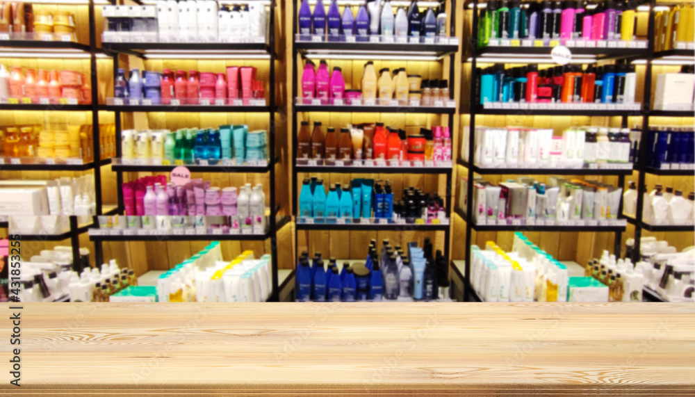 Mock up template, wooden table top, desk top counter in foreground for your product or text. Defocused blurred image of shelves with cosmetics, shampoos and creams in a cosmetics store.