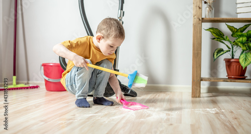Fotografia Little boy is sweeping the trash from the floor with a broom to a dustpan
