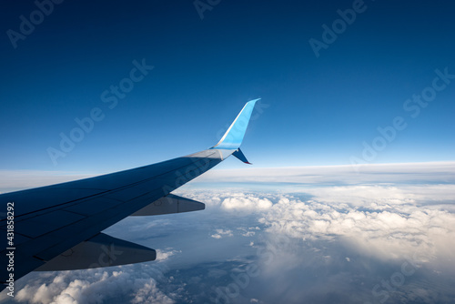 Commercial airplane while flying above the clouds and clear blue sky. Looking through the plane window.