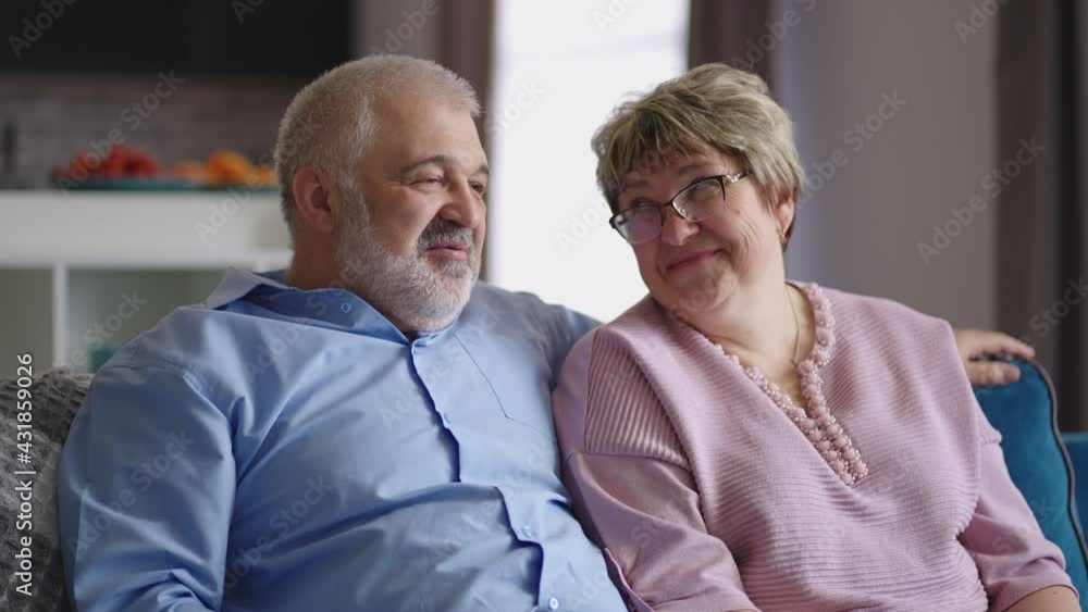 happy granny and grandpa are sitting on couch in apartment and talking cheerfully, retirees are resting at home at weekend happy granny and grandpa are sitting on couch in apartment and talking cheerfully, retirees are resting at home at weekend