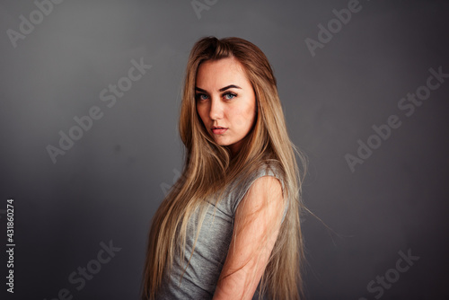 A girl with blue eyes looks piercingly into the frame, wrapping her hair in a gray background