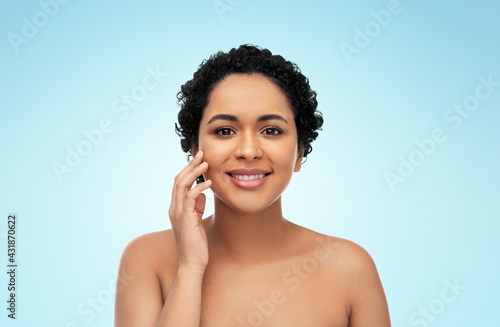 beauty and people concept - portrait of happy smiling young african american woman with bare shoulders touching her face over blue background