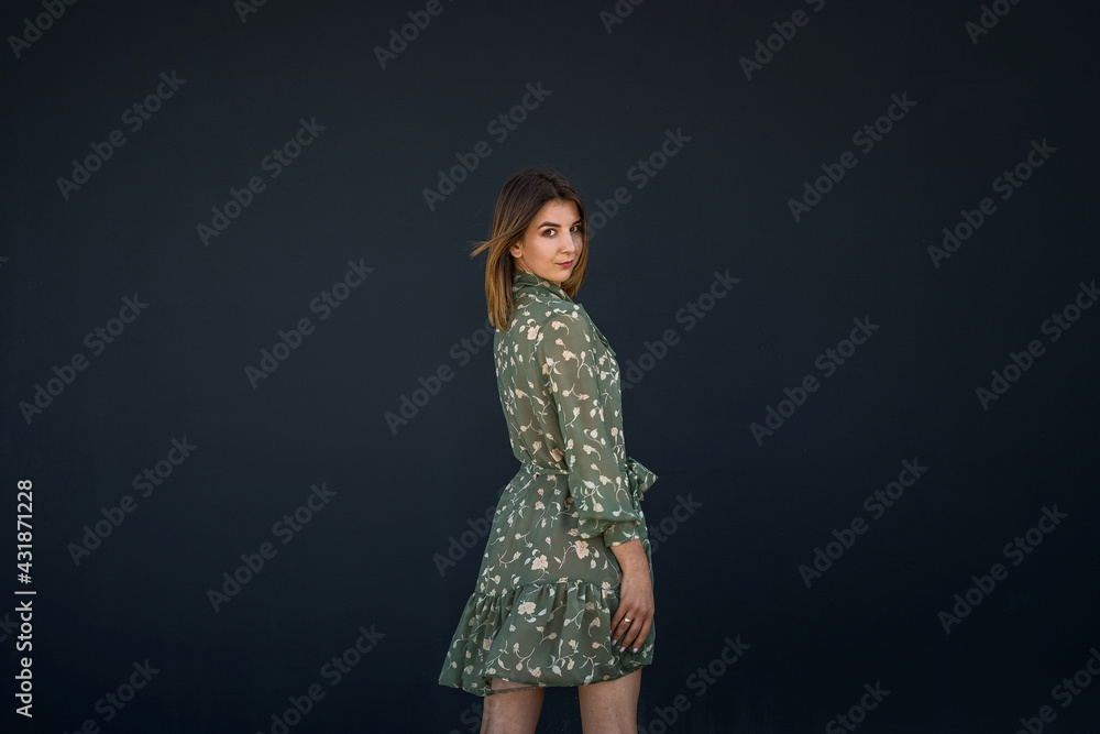 Calm beautiful young woman in elegant green dress near black wall Calm beautiful young woman in elegant green dress near black wall