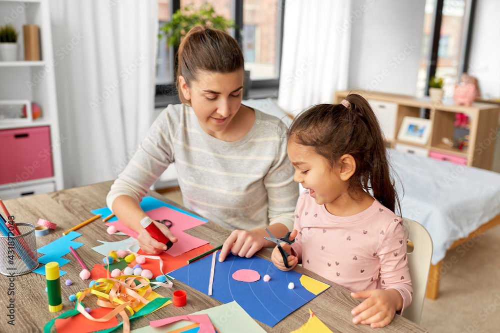 Fototapeta premium family, art and craft concept - mother spending time with her little daughter with glue making applique of color paper at home
