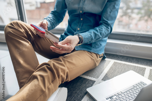 Close up picture of a man sitting on the window with a credit card in hands