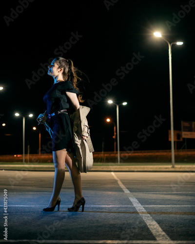 Girl in a coat in the parking lot against the backdrop of the night city with lanterns photo