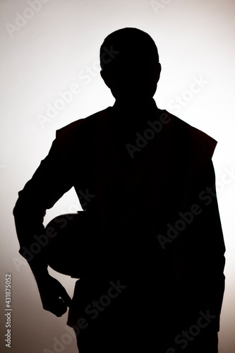 male silhouette of construction worker figure with hard hat under arm on studio background, building industry concept