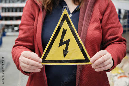 Woman holds yellow triangular sign with lightning bolt painted on it. The sign warns of high electrical voltage. Concept of warning signs and mandatory compliance with occupational safety regulations