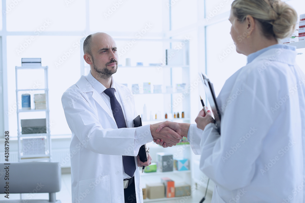 Pharmacists is Working. Man and Woman Handshaking with Each Other. Persons is Smiling. People Wearing Special Medical Uniform. People Located in Pharmacy. Pharmacists is Working. Man and Woman Handshaking with Each Other. Persons is Smiling. People Wearing Special Medical Uniform. People Located in Pharmacy.