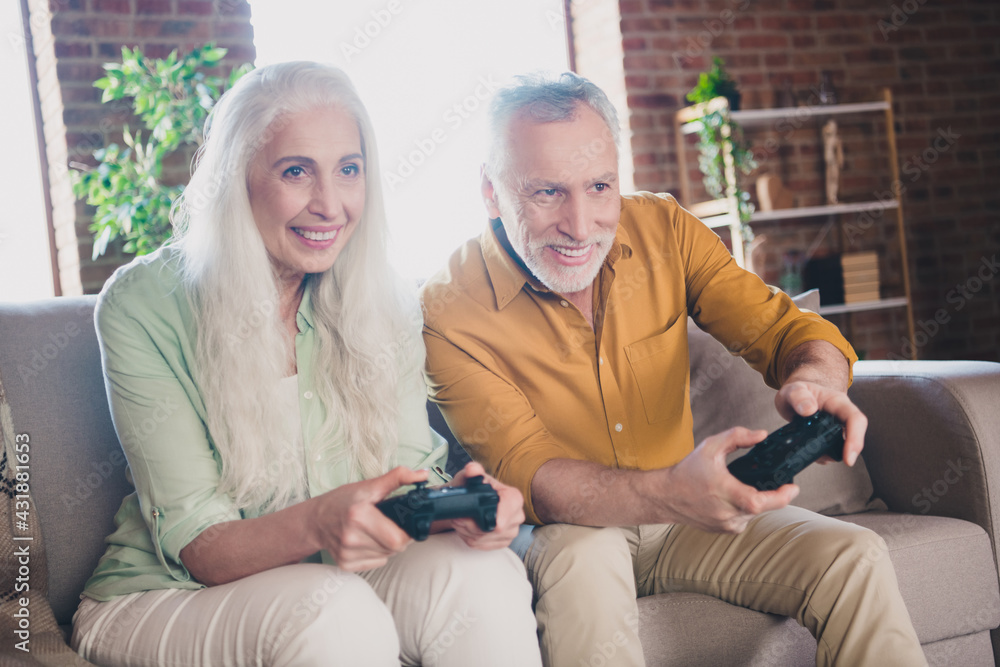 Photo of pretty funky pensioner lady gentleman sitting couch enjoying playstation smiling indoors house flat