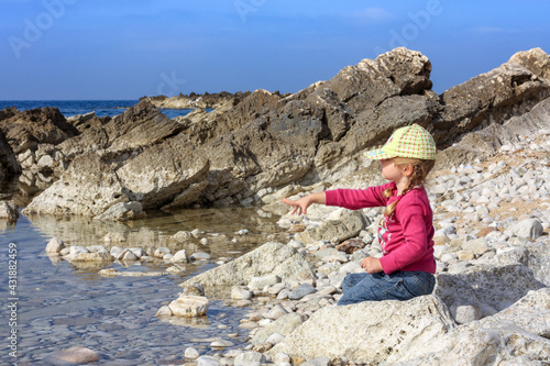 Bambina al mare che gioca tirando sassolini