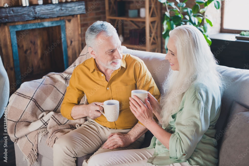 Photo of positive charming man and woman old people good mood sit sofa drink tea indoors inside house home - obrazy, fototapety, plakaty 