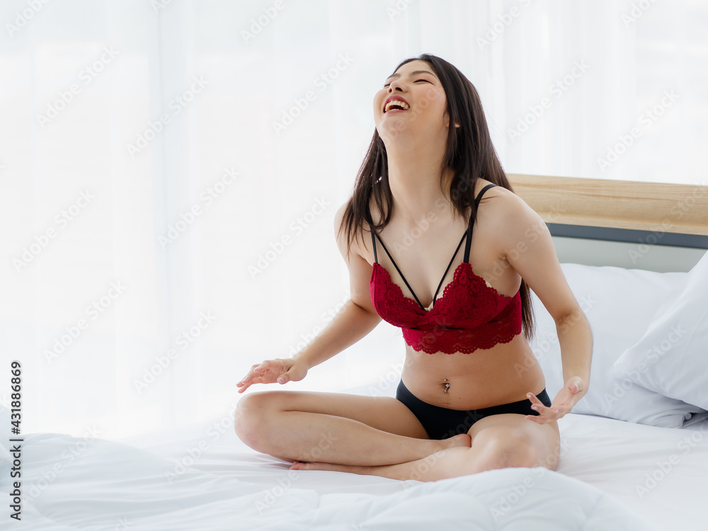 Obraz premium Beautiful young naughty sexy girl with romantic underwear cross-legged sit on white bed and laughing as she trying to so something funny in bright morning of rest day