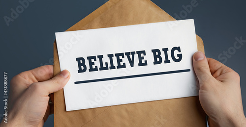 Wallpaper Mural Closeup of a male hands holding craft envelope with text Believe BIG on blue background Torontodigital.ca